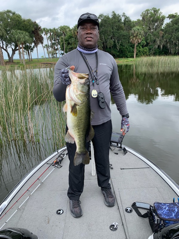 Man standing on a boat holding a largemouth bass vertically that weighs 8 pounds 1 ounce