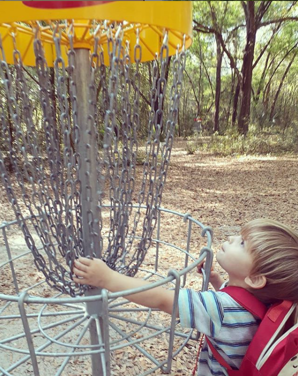 kid with hand in disc golf basket