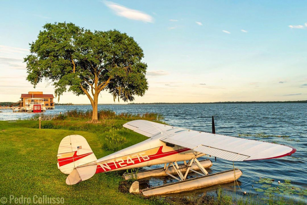 Seaplane parked on the bank of a lake with a building in the background.