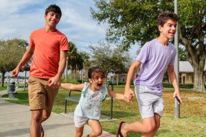 Three siblings run at a park.