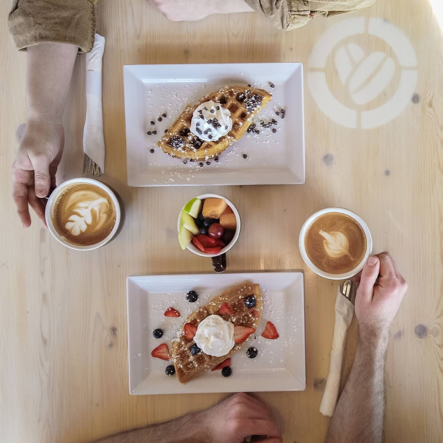 Photo of two waffle breakfasts and 2 coffees from above. 