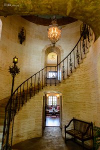 Grand staircase inside mansion. Light colored bricks and iron railing. 